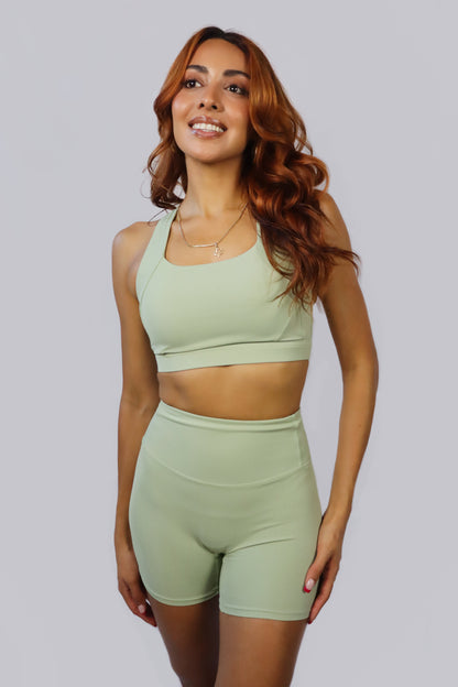 Woman wearing a green sports bra and shorts set on a light gray background