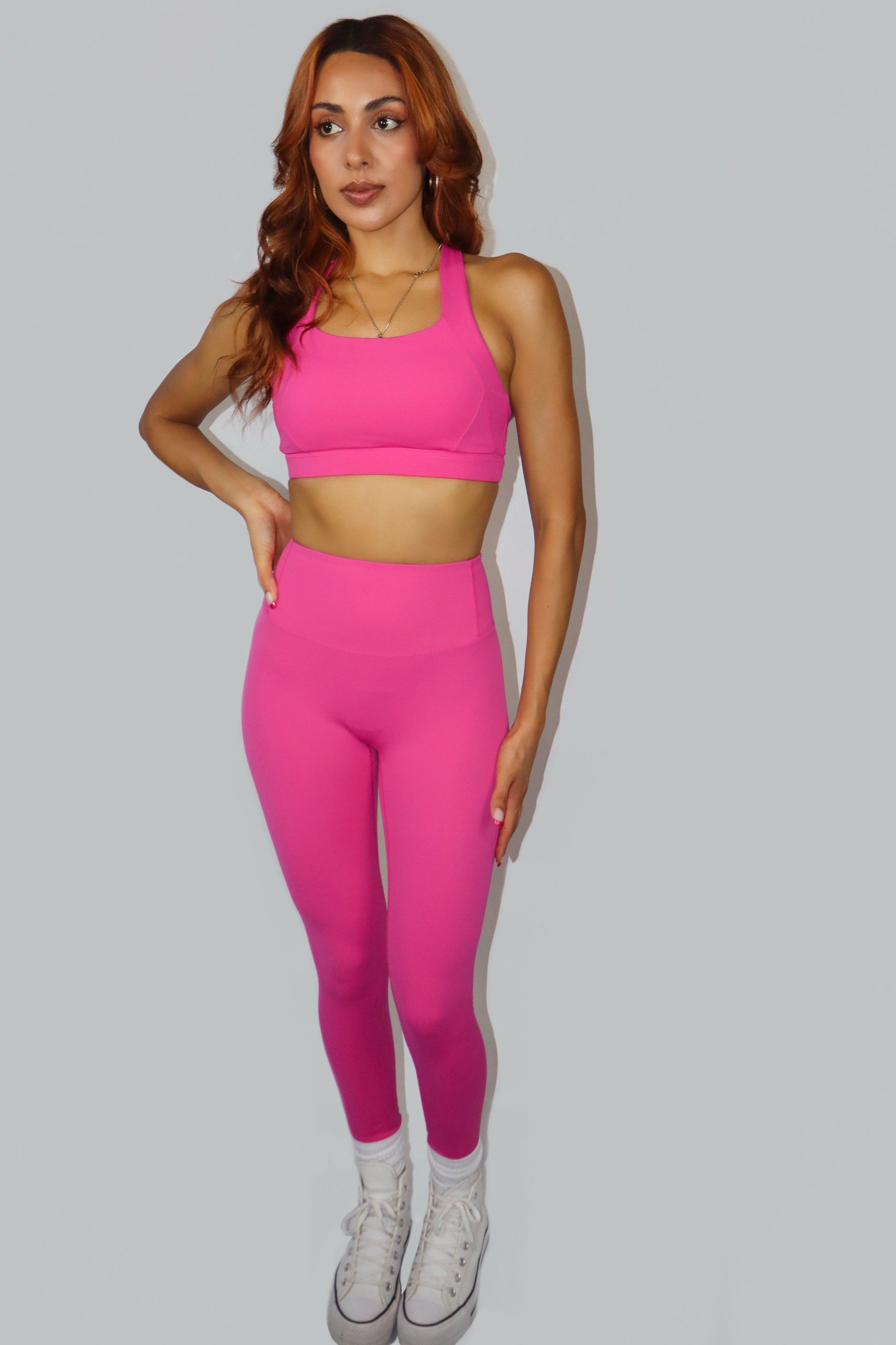 Woman wearing a pink sports bra and leggings set on a gray background