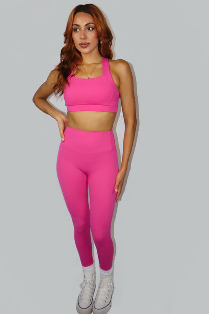 Woman wearing a pink sports bra and leggings set on a gray background