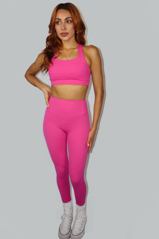 Woman wearing a pink sports bra and leggings set on a gray background