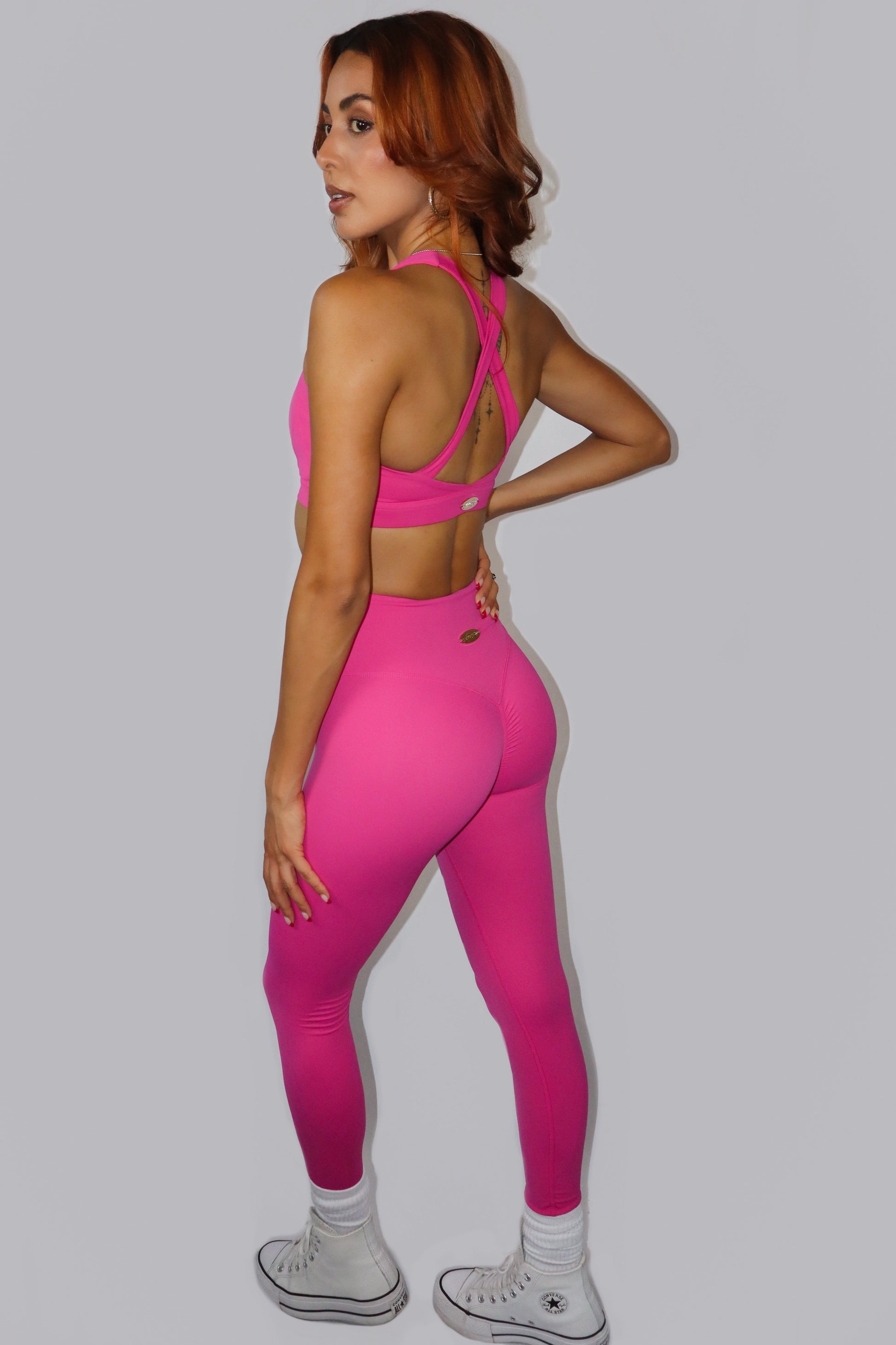 Woman wearing a bright pink sports bra and leggings on a plain background