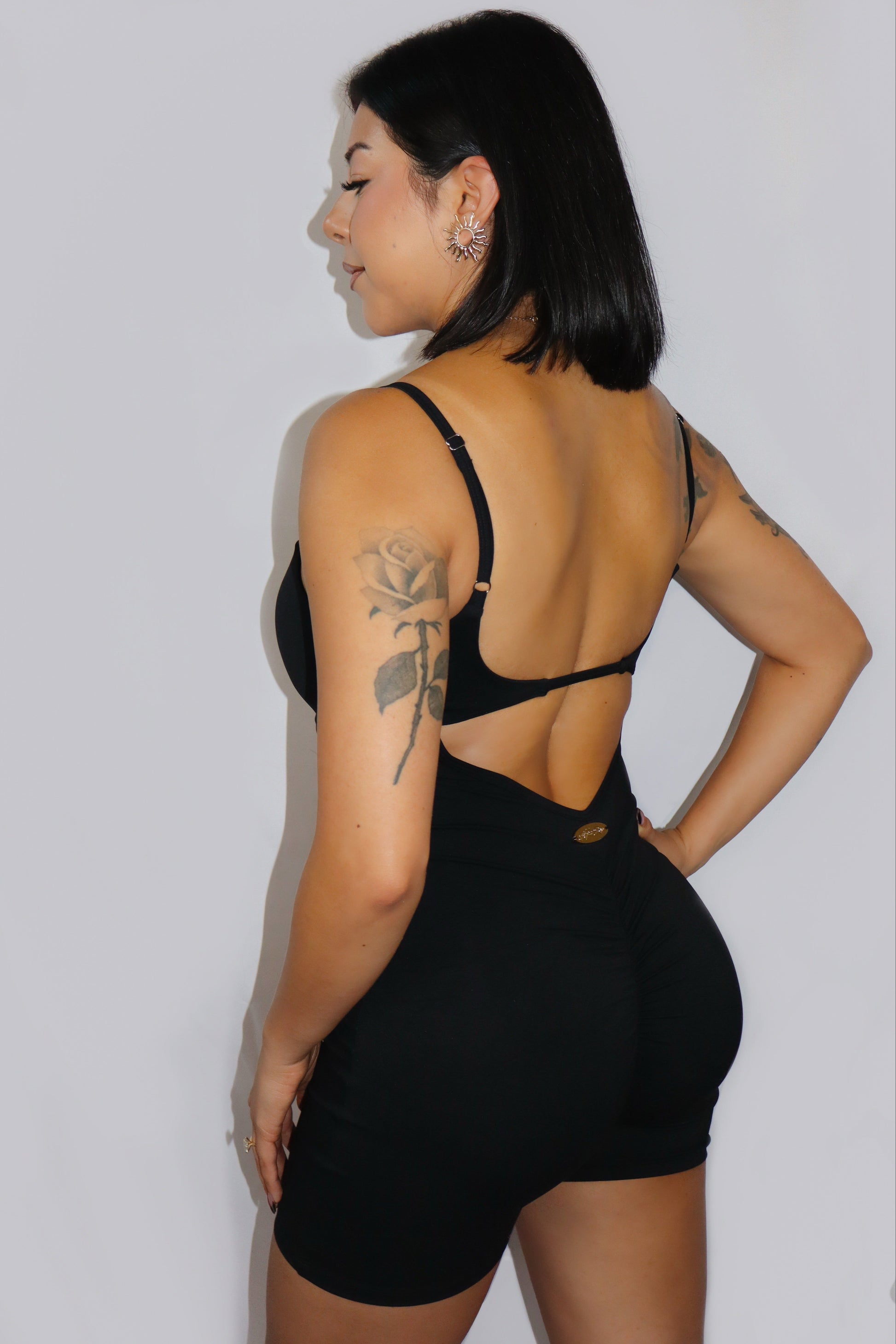 Woman wearing a black open-back romper against a plain background