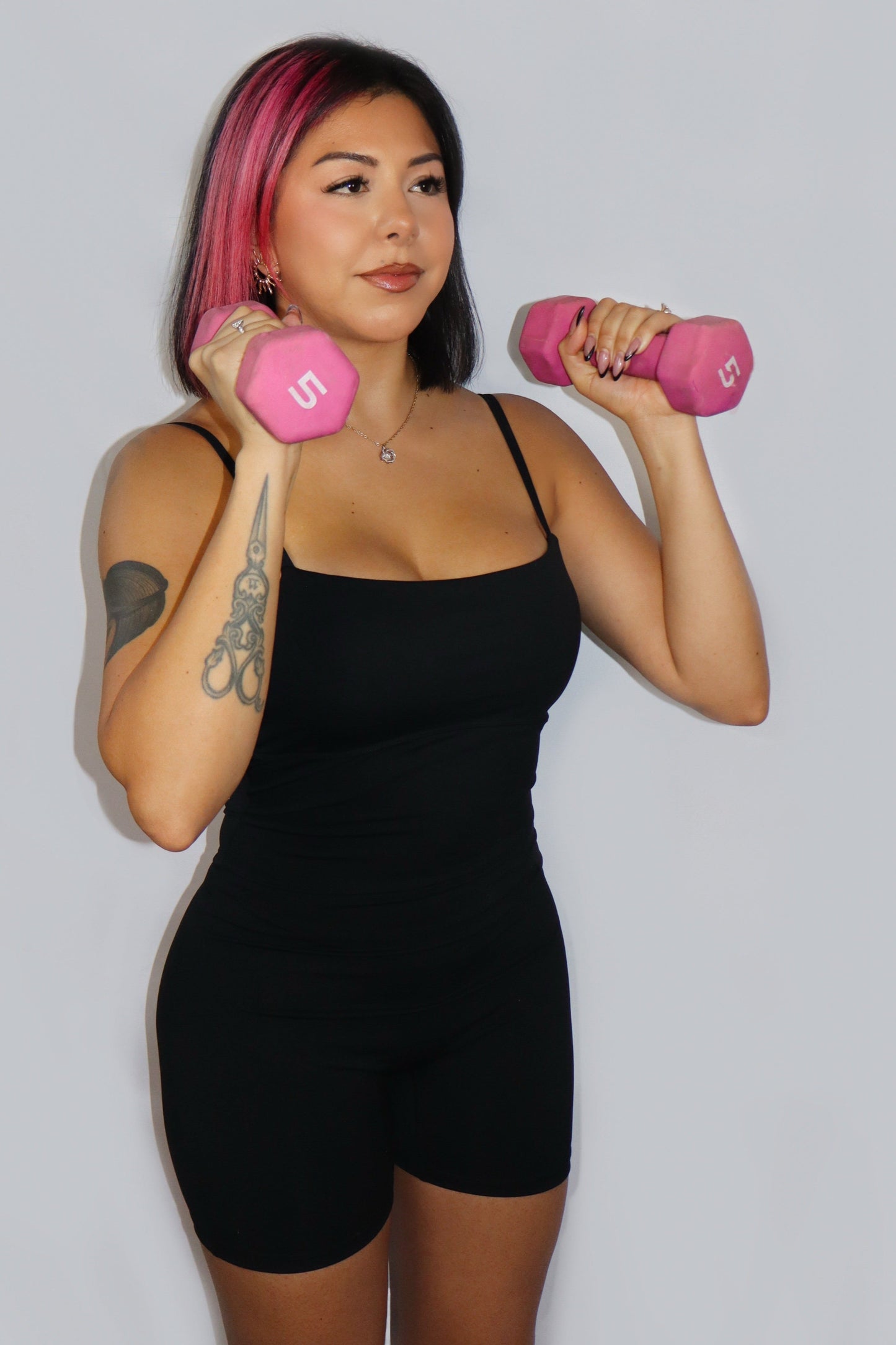 Woman holding pink dumbbells against a plain background