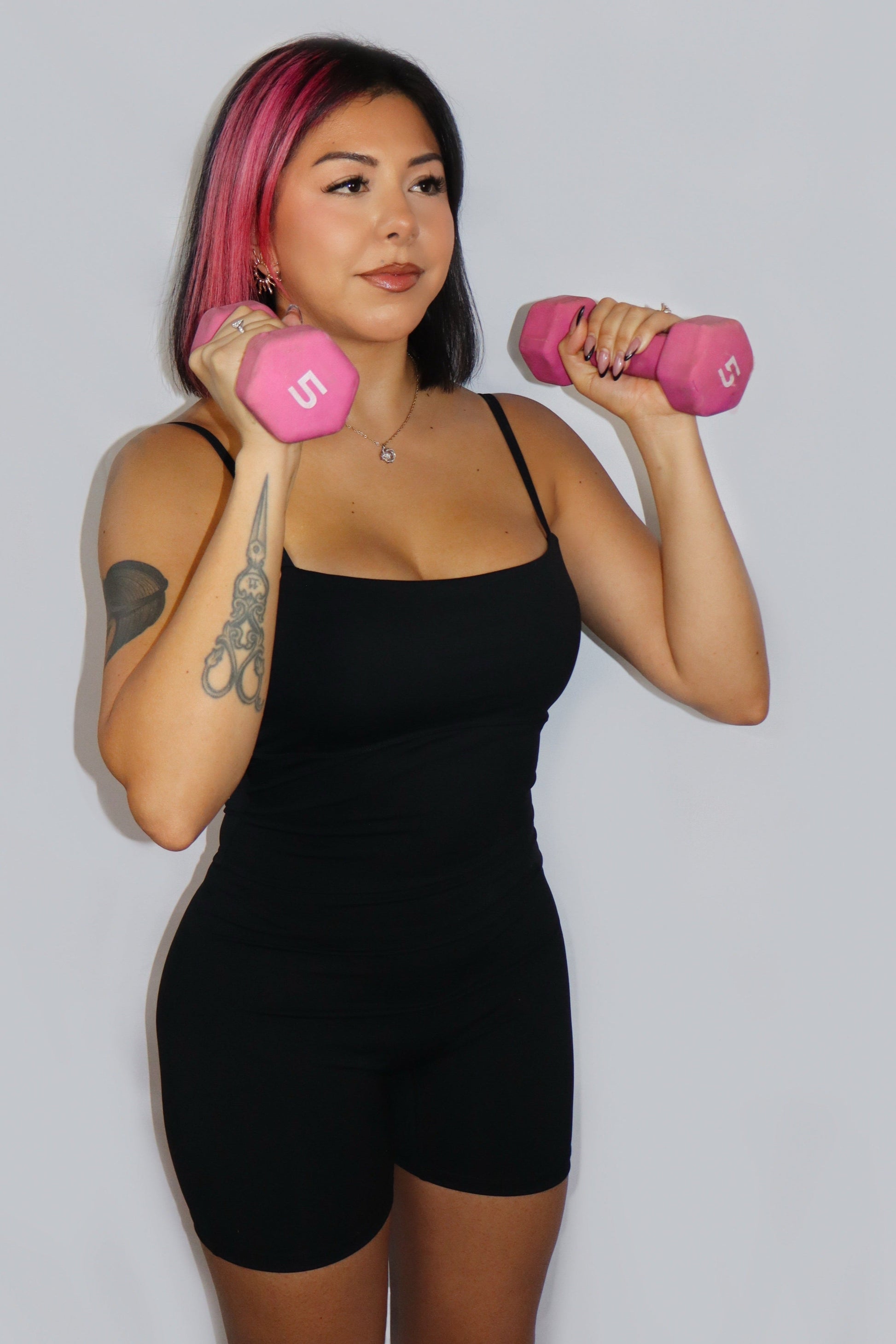 Woman holding pink dumbbells against a plain background