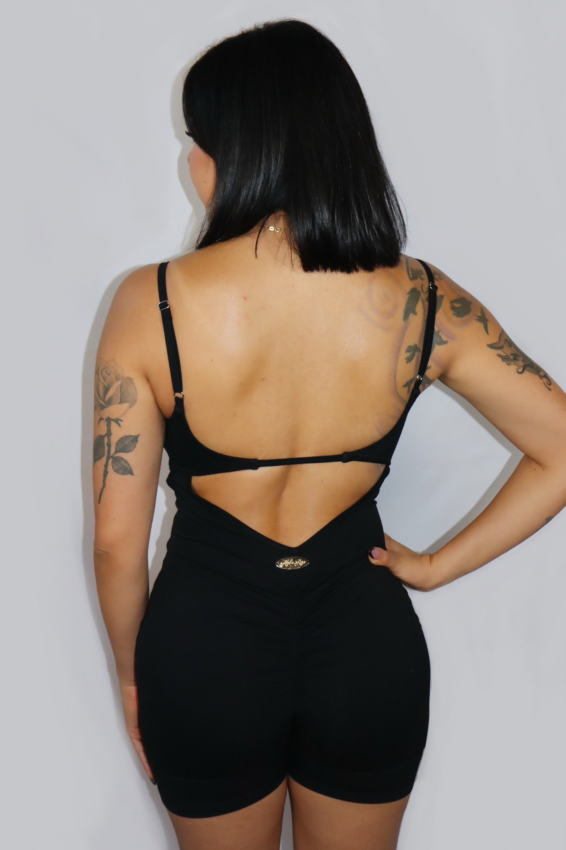 Person wearing a black open-back romper against a plain background