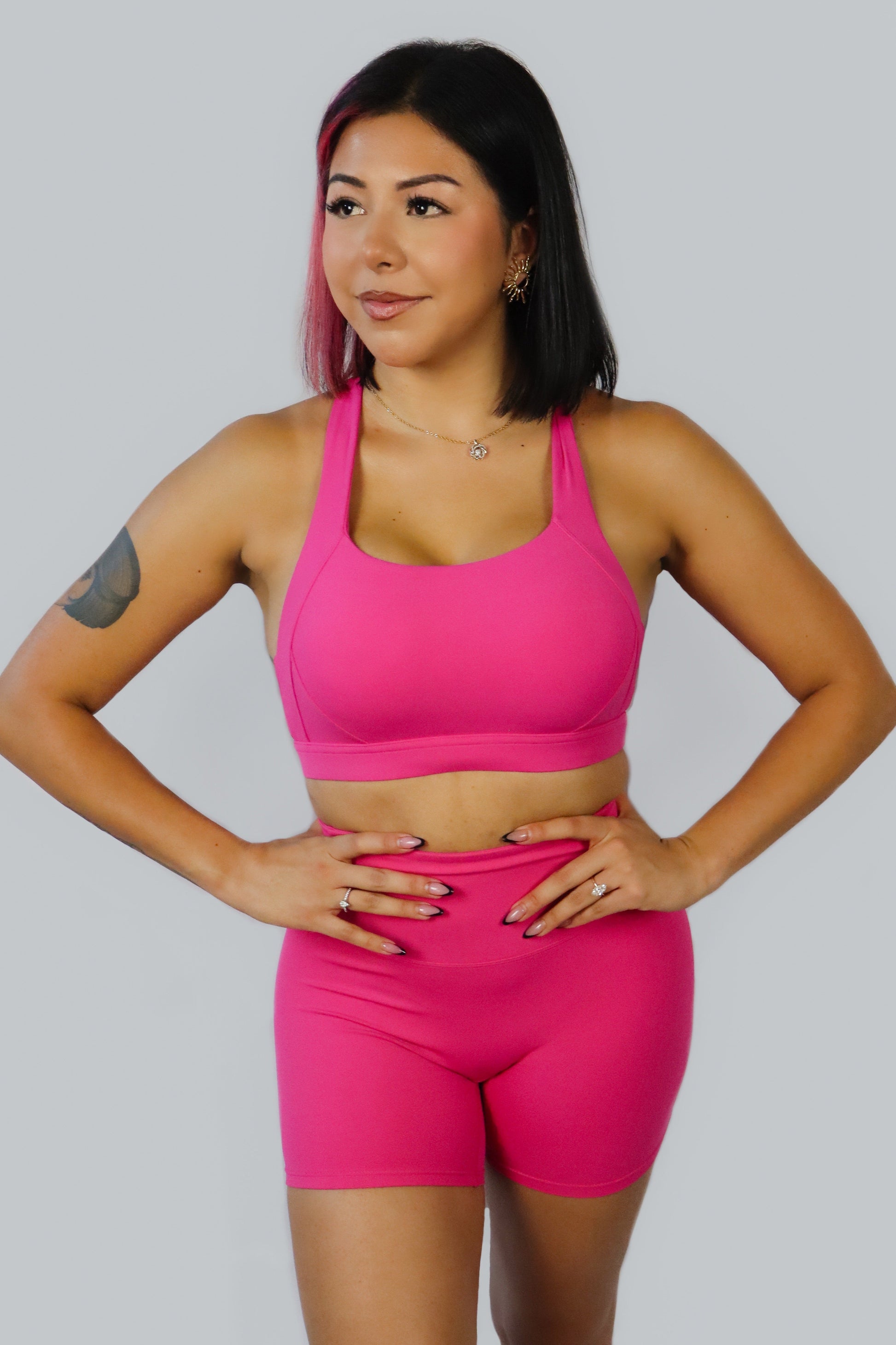 Woman wearing a bright pink sports bra and shorts set on a plain background