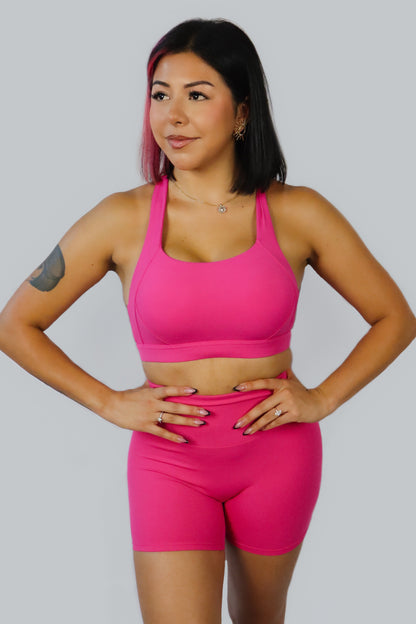 Woman wearing a bright pink sports bra and shorts set on a plain background