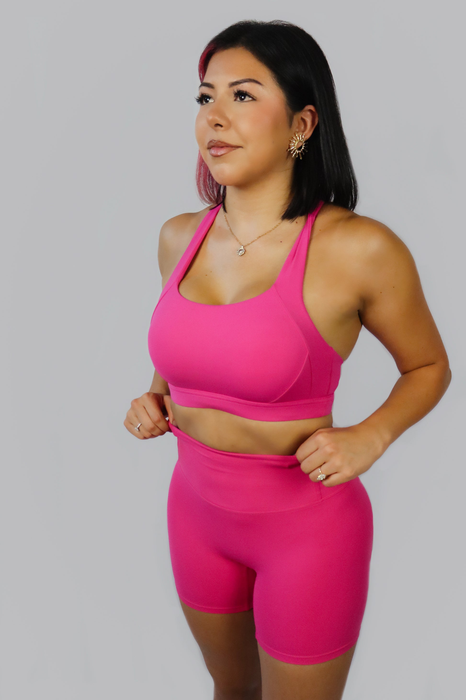Woman wearing a bright pink sports bra and shorts set on a gray background